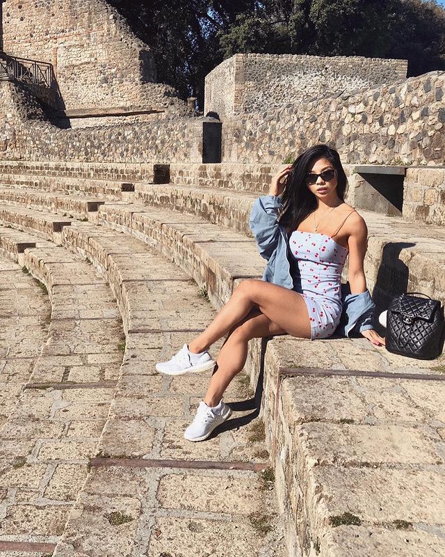 Lexi Vixi posing in sun wearing a light blue bodycon dress and tinted sunglasses